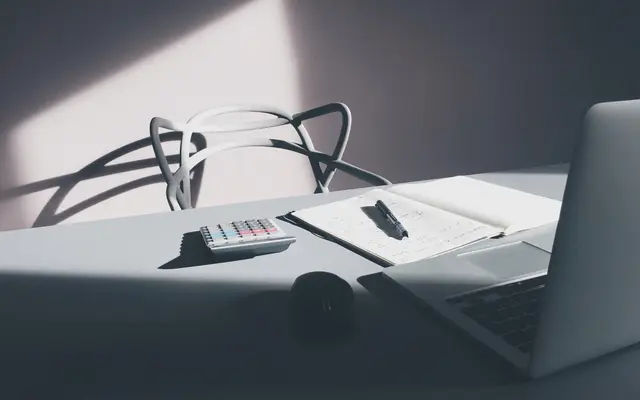 Laptop, calculator and open notebook with handwritten working on a desk in soft window light