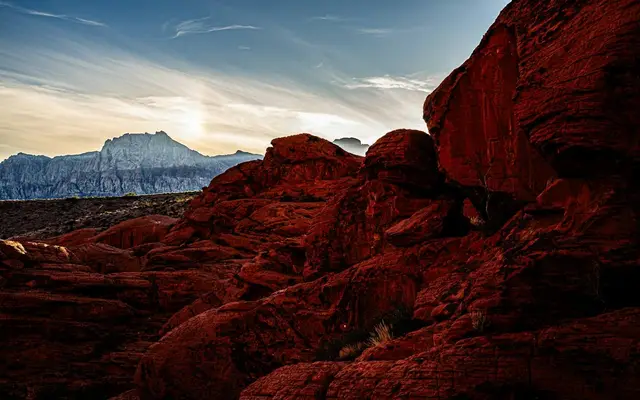Red sandstone boulders in shadow at Red Rock Canyon, Nevada, with a pale limestone ridge under a streaked evening sky