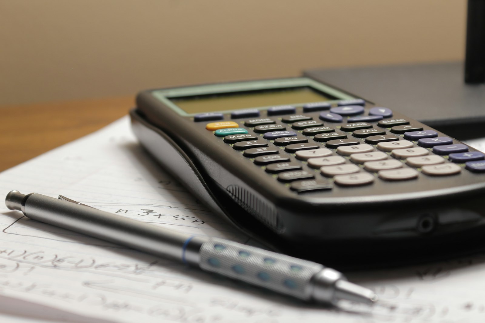 A graphing calculator and mechanical pencil resting on handwritten maths notes